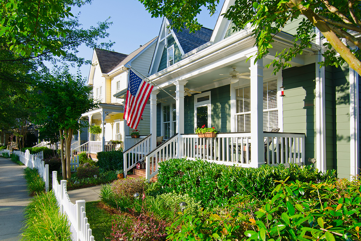 The quintessential American Dream: A house with a white picket fence and American flag hanging from the porch