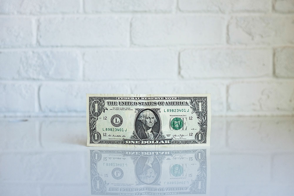 A one dollar bill on a white table with a white brick wall in the background