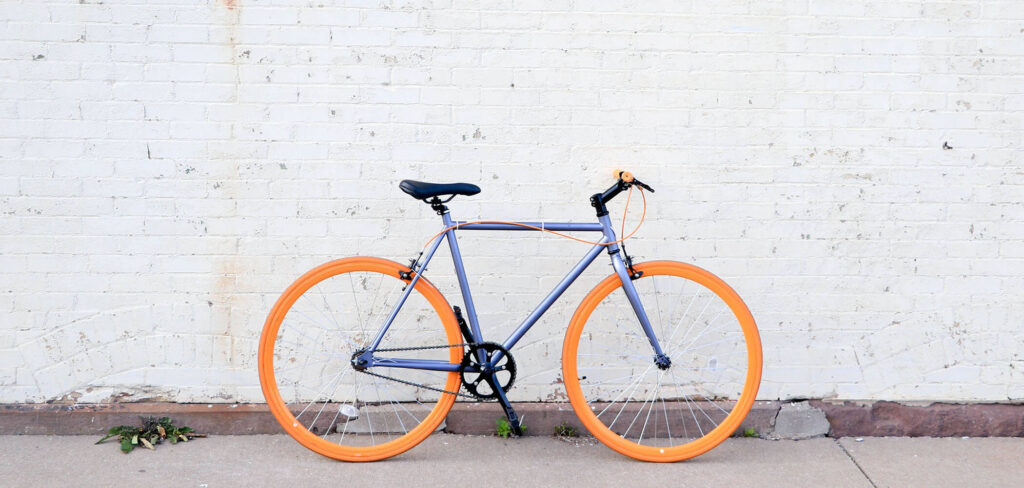 A brightly colored road bike on a sidewalk against a whitewashed brick wall