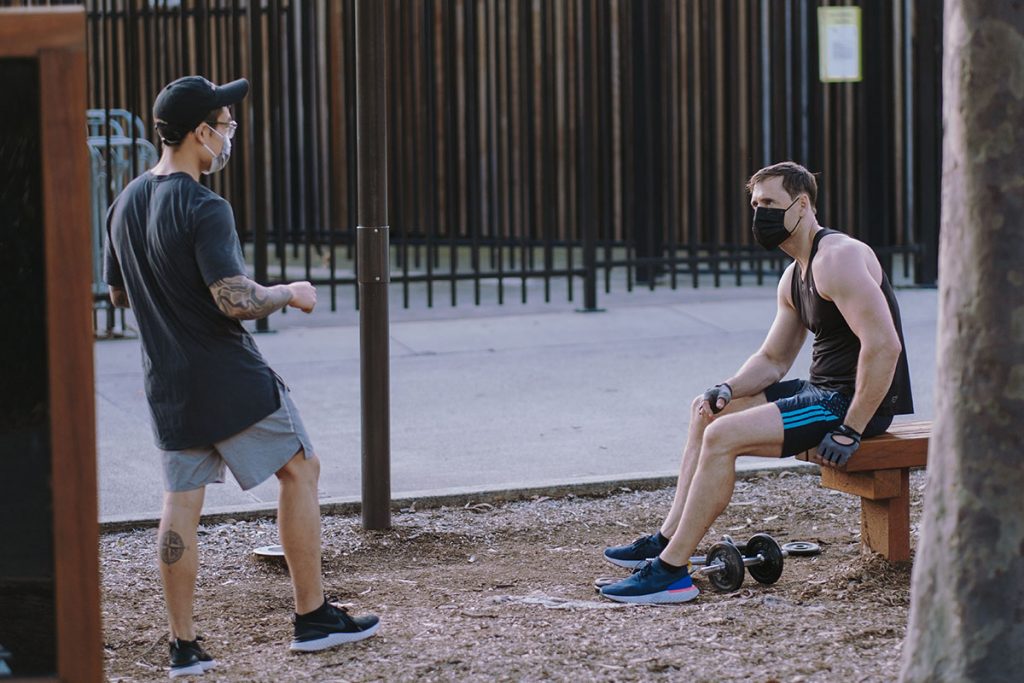 Two men in a public park talking at a safe distance, both wearing masks