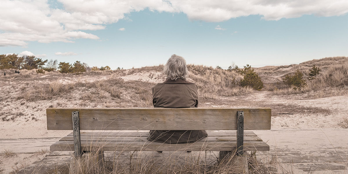 The State of Americans Mental Health: an elderly person sits on a bench near a beach