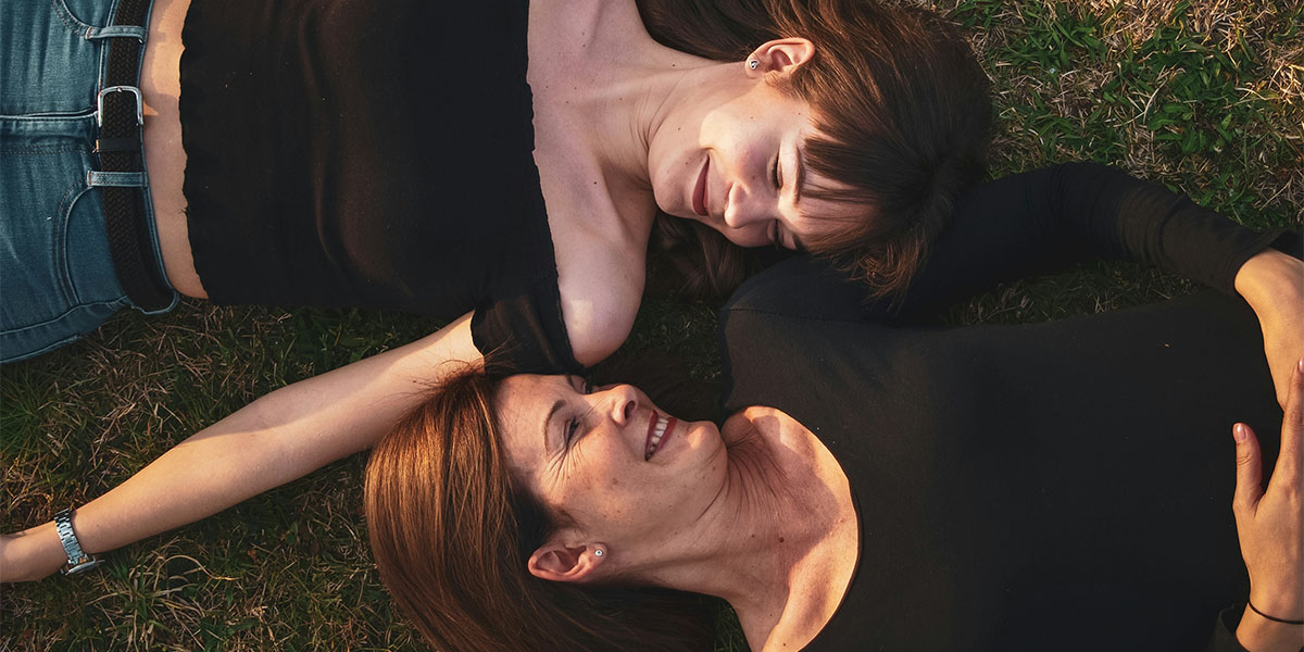 A mother and daughter lie on the grass, looking at each other