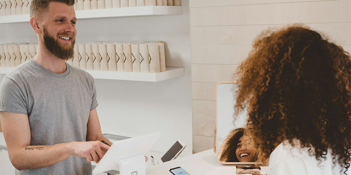 Man working in retail space smiles to female customer ready to make a purchase