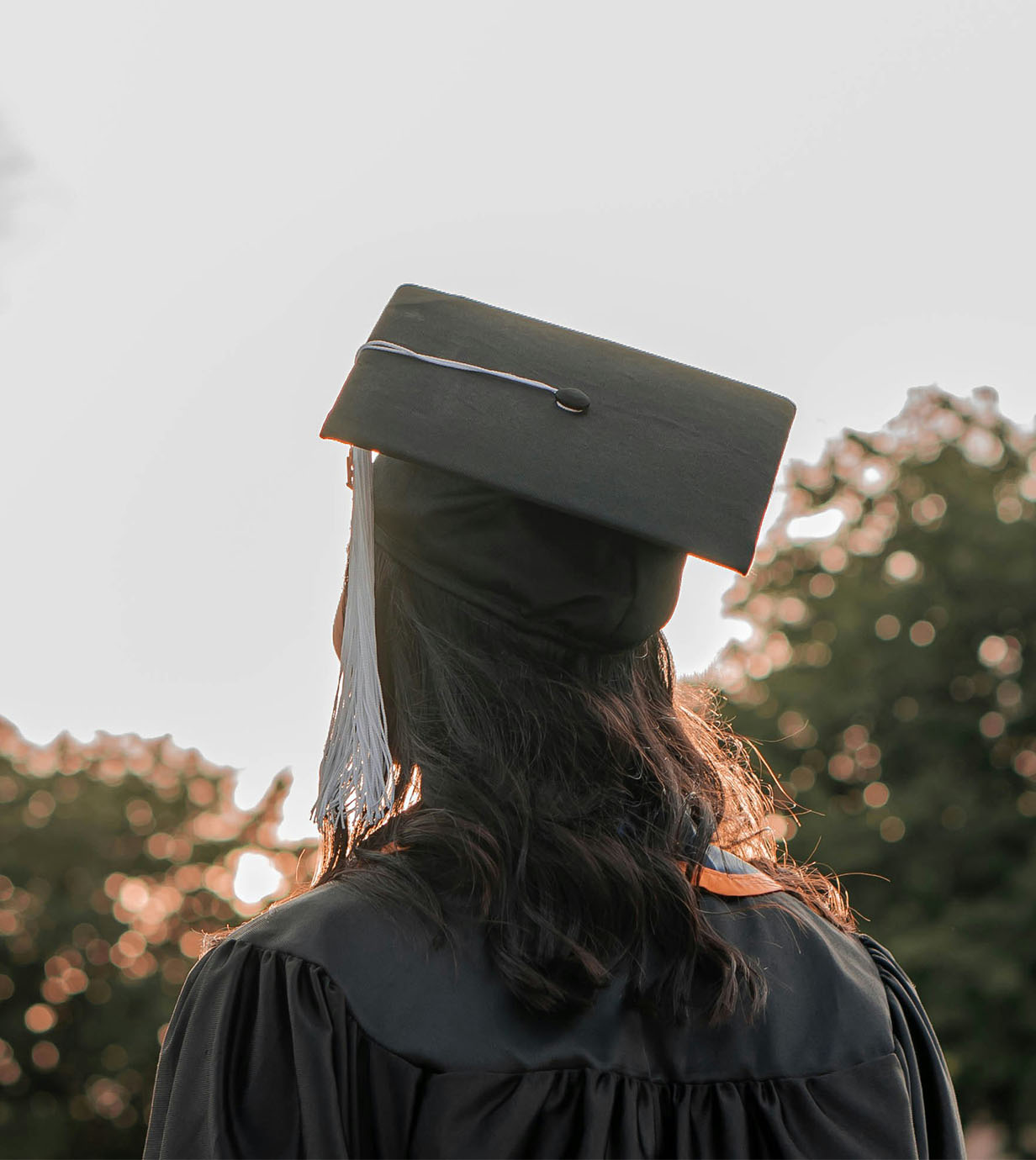 Entry level hiring case study: a recent grad looks away, over distant trees, wearing cap and gown